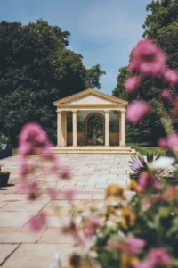 A classical garden pavilion framed by blooming flowers, set within the landscaped grounds of Rowton Castle on a bright summer day.